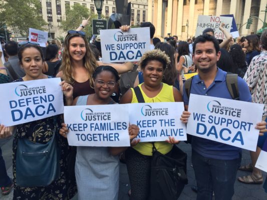 Five MFJ attorneys hold up signs at a Foley Square demonstration in support of DACA. Signs read: Defend DACA; Keep Families Together; Keep the Dream Alive; We Support DACA.